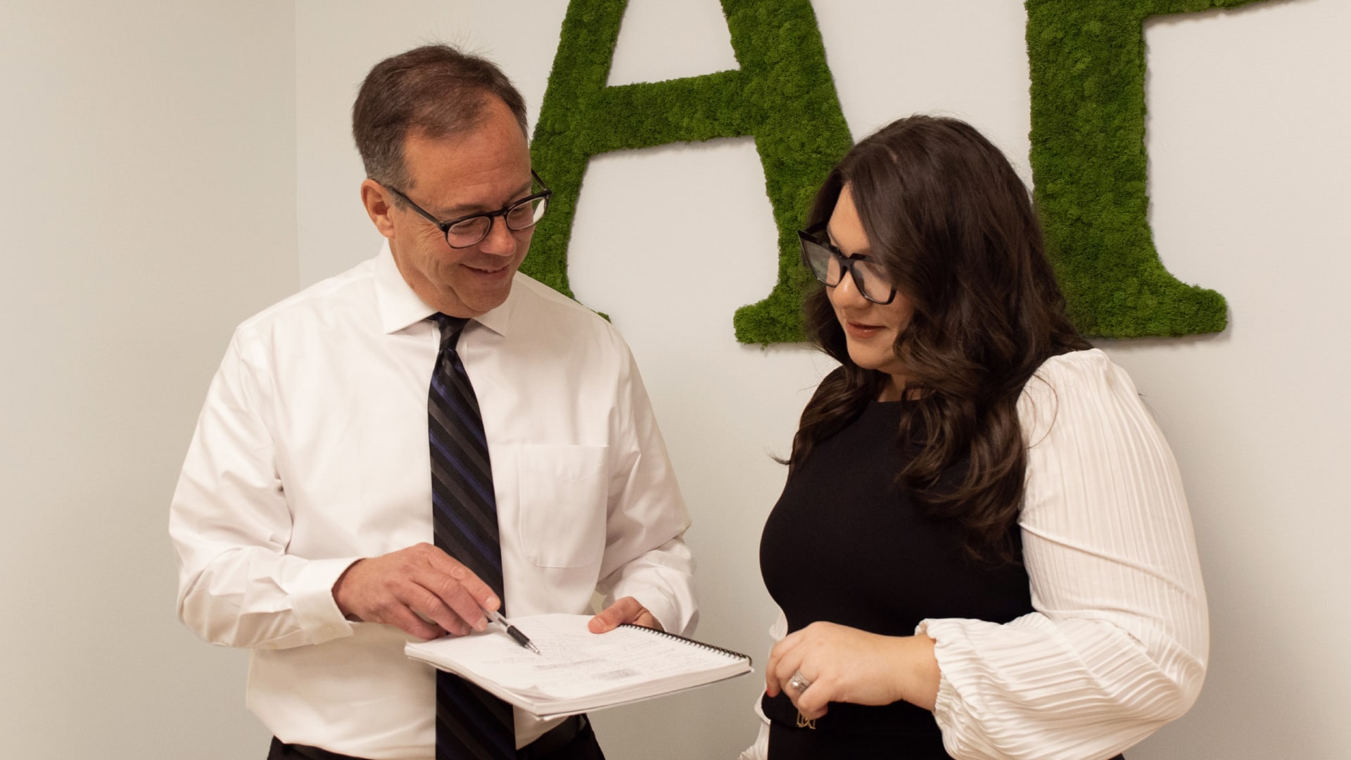 two people having a conversation in business attire. man point to paper with pen.